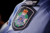 Queensland Police Service logo on shoulder sleeve of officer's shirt.