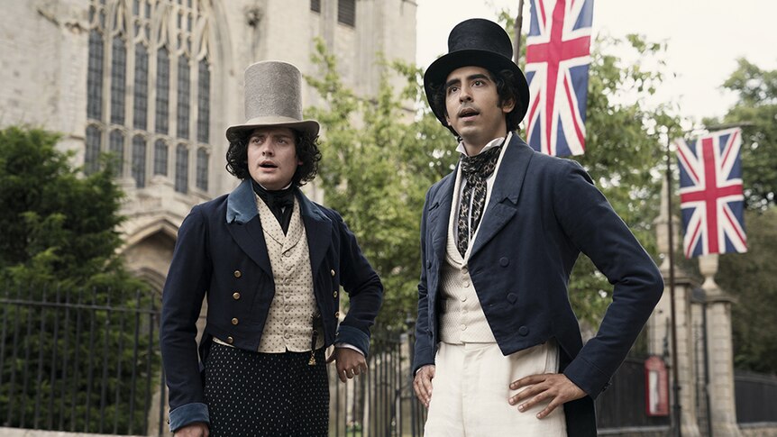 Two men in top hats and Victorian era suits look surprised and stand in in front of building with union jack flags at gates.