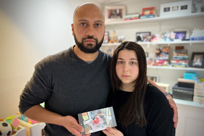 A man and woman wearing black and holding up a photo frame with a little boy pictured.