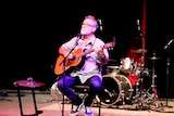 Man looks up to crowds as he plays guitar on a stage.