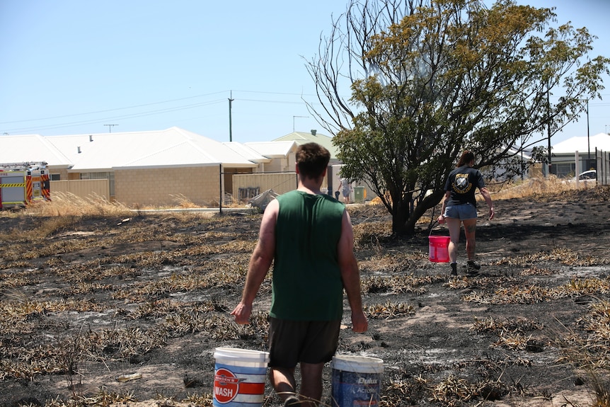 Residents cart buckets of water through a fire ground