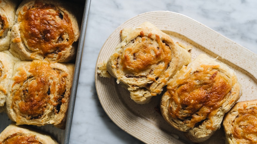 A tray of freshly baked cheese and Vegemite scrolls, with three scrolls on a plate, a tasty savoury snack.