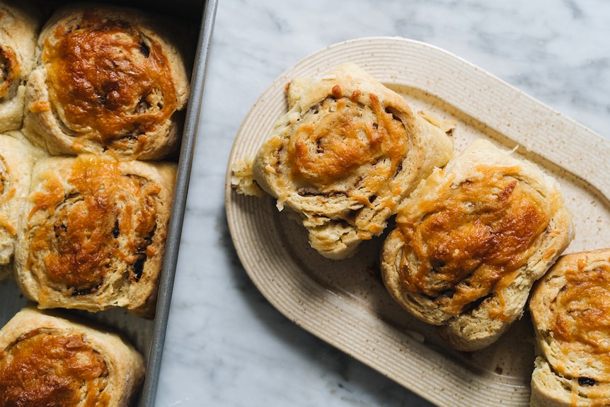 A tray of freshly baked cheese and Vegemite scrolls, with three scrolls on a plate, a tasty savoury snack.