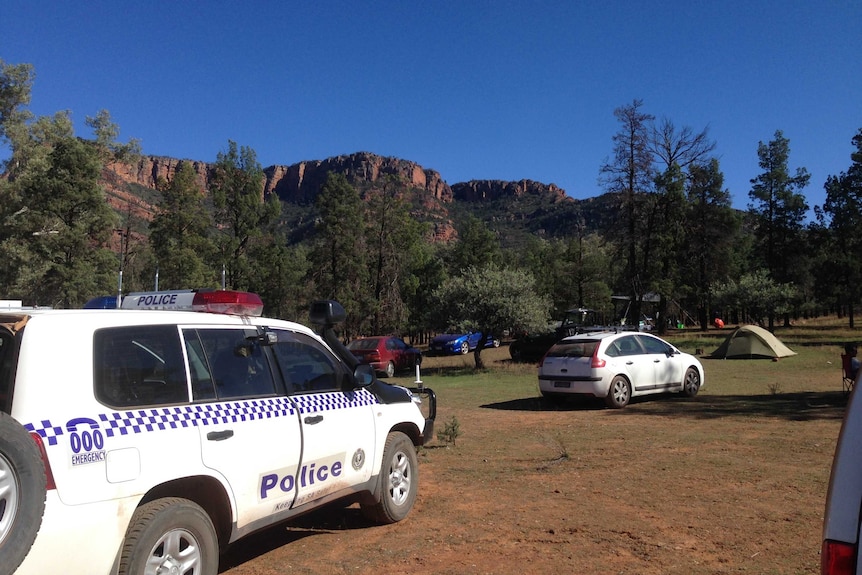 A police four-wheel drive is parked near tents and other cars.