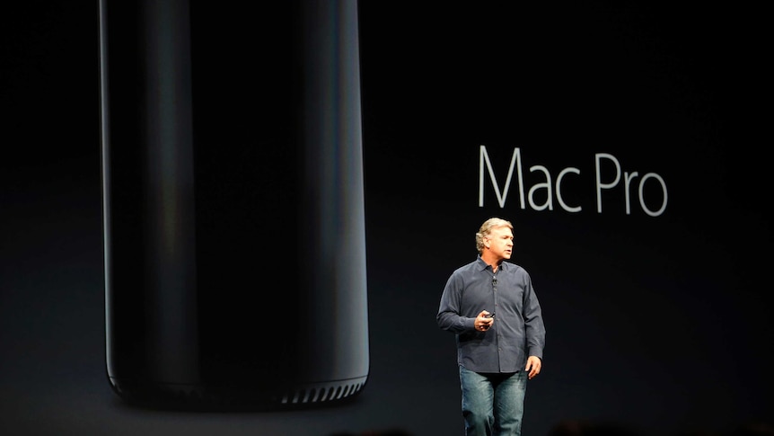 Phil Schiller on a darkened stage with slideshow showing the new Mac Pro behind him.