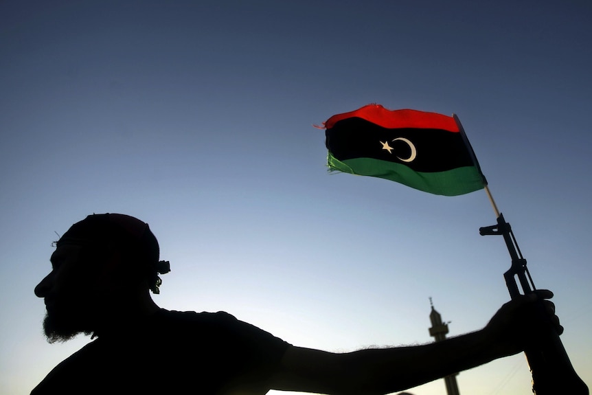 A Libyan new regimes forces fighter holds a weapon with a Libyan flag