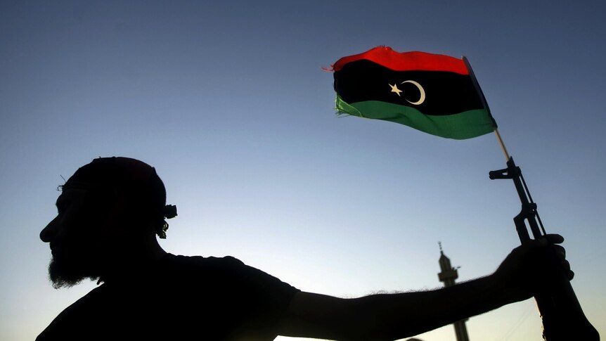 A Libyan new regimes forces fighter holds a weapon with a Libyan flag