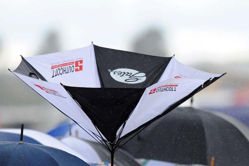 An umbrella is turned inside out in a crowd of people wearing ponchos and carrying other umbrellas.