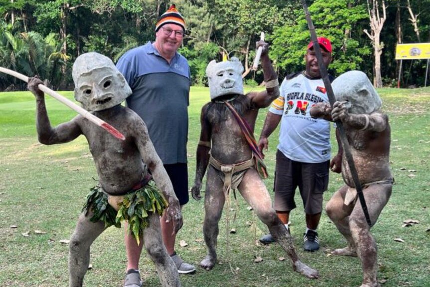 Don Matheson and a group of PNG Mudmen holding spears stand on a field. 