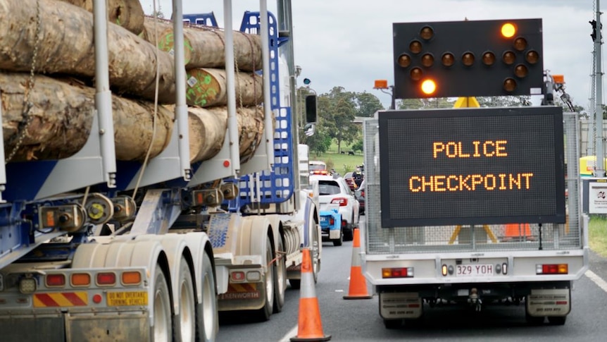 A logging truck waits behind a line of cars alongside a "police checkpoint" sign.
