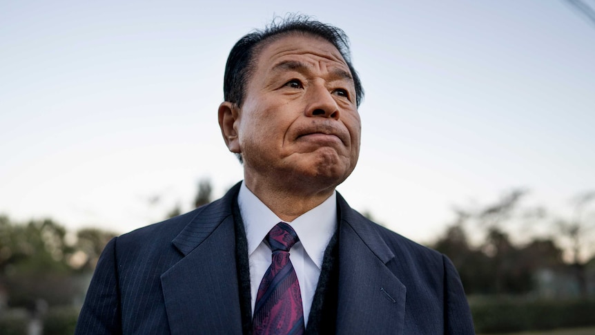 Takeshi Tsuchida in a suit and coat with a grim expression