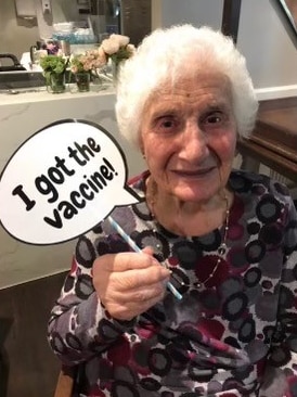 Elderly woman holds up a sign saying 'I got the vaccine'. 