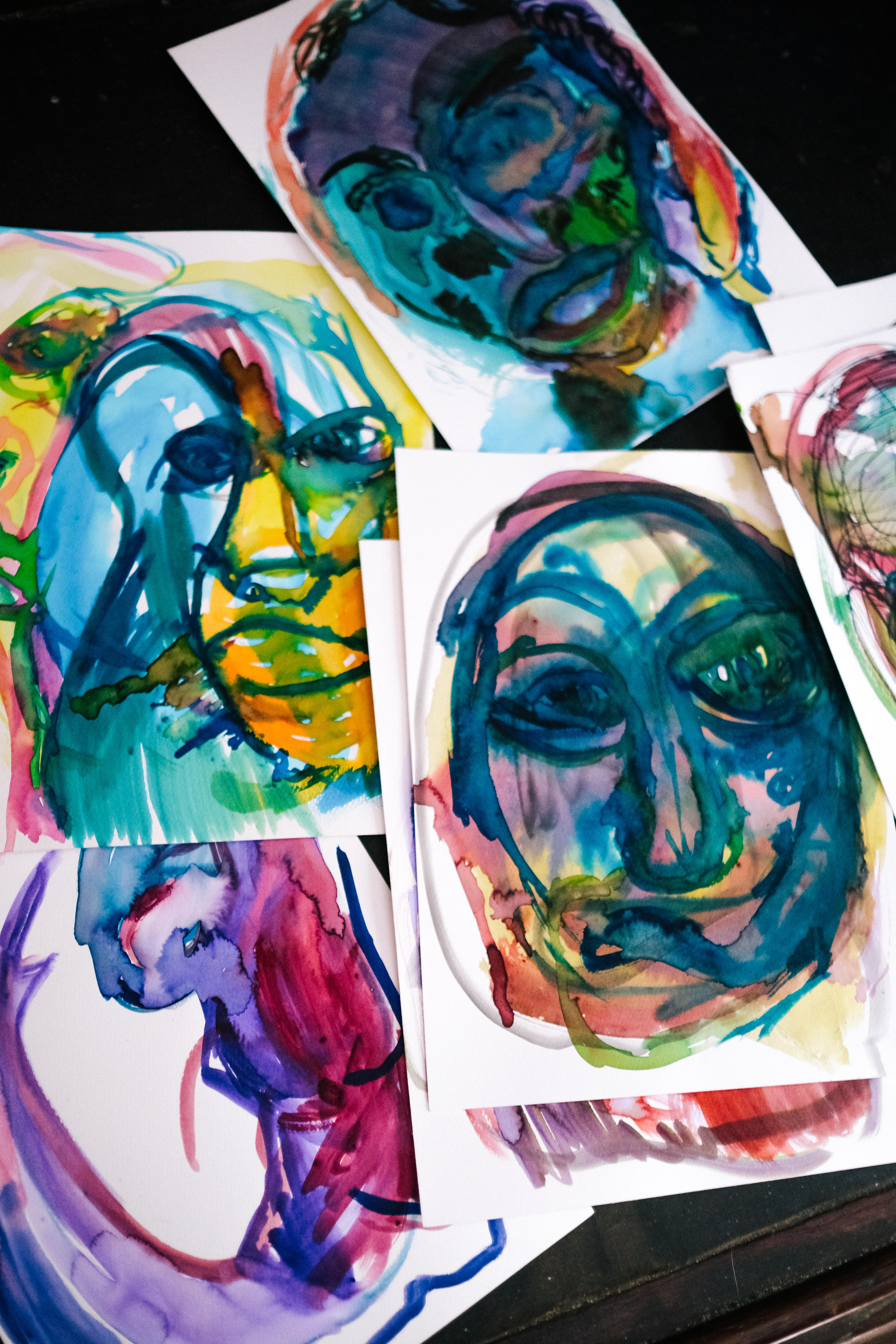 Five colourful watercolour paintings by Walker spread out on a table. They feature abstract, distorted faces.