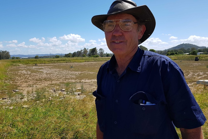 man in hat stands front of a dry pond which used to stock prawns