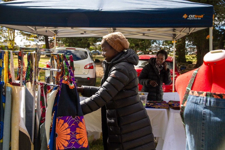 Two women stand with an apron stall at an outdoor market.