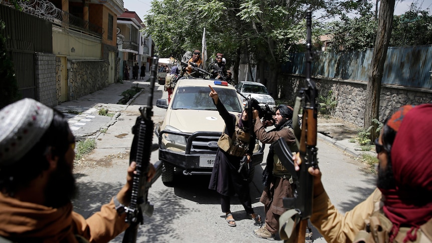 Taliban fighters hold up weapons while sitting in the back of a vehicle.