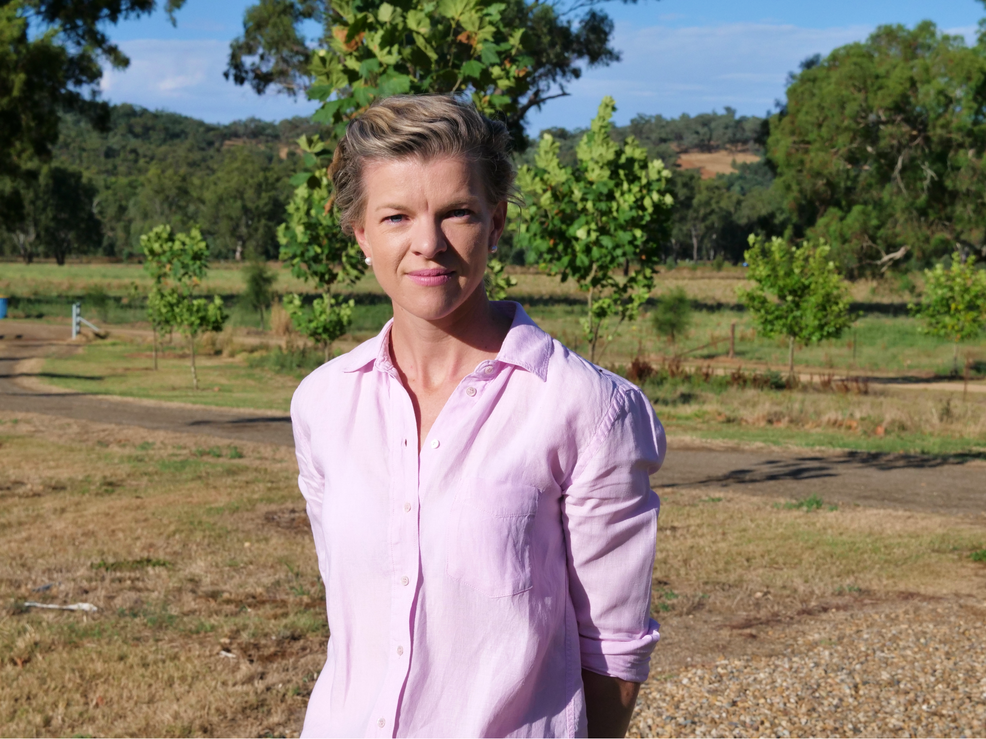 Doctor in pink shirt with blonde hair and blue eyes looks into the camera against a country NSW background in Wagga Wagga
