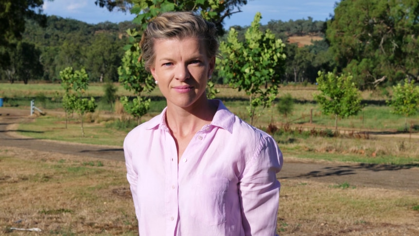 Doctor in pink shirt with blonde hair and blue eyes looks into the camera against a country NSW background in Wagga Wagga