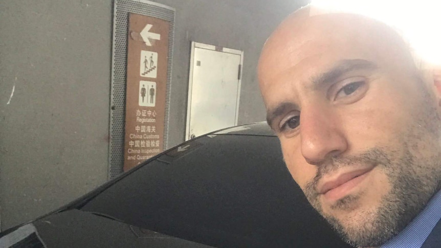 Stavro D'Amore, with bald head and facial hair, takes a selfie in front of a black sedan.