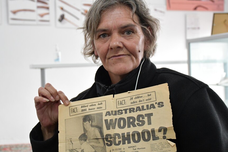 A woman holds an aged newspaper clipping that says "Australia's worst school?"