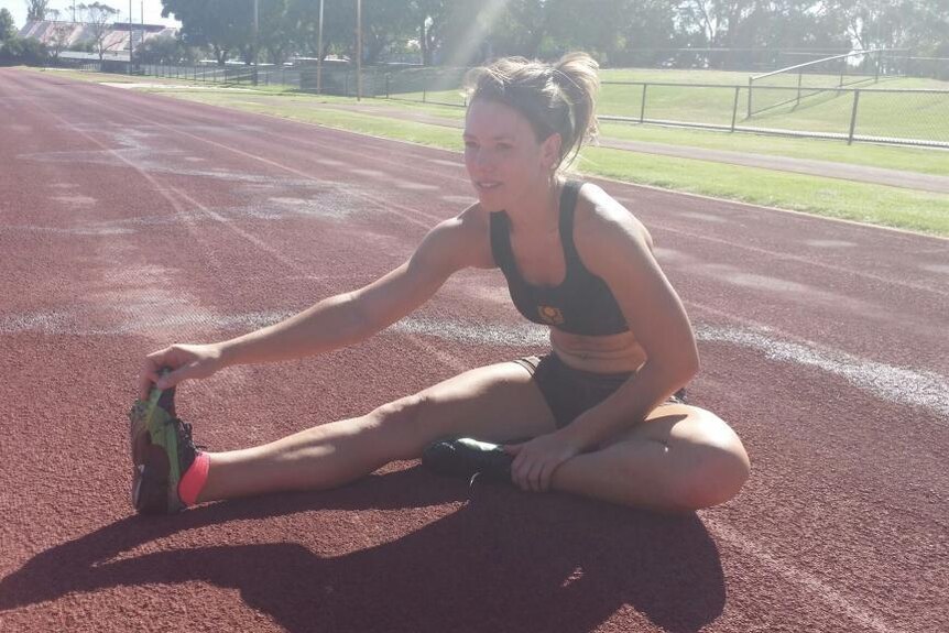 A young woman stretching her legs on an athletics track