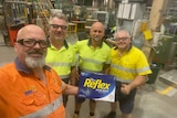 Four men in high-vis fluro shirts stand smiling with a package of white, A4 paper. 
