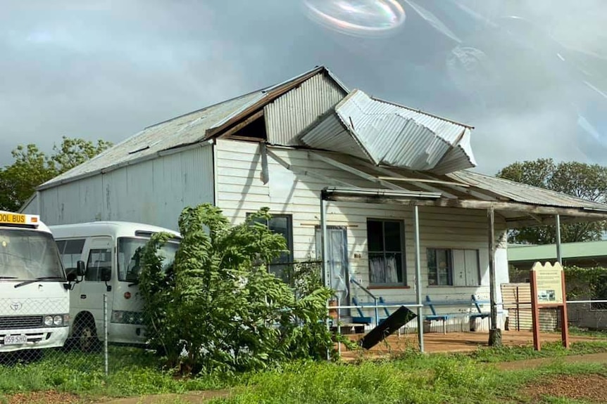 A house with a mangled tin roof, a tree is also damaged.