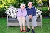 A portrait of Audrey MacGregor and her husband of 61 years, Walter sitting on a lounge in a garden.