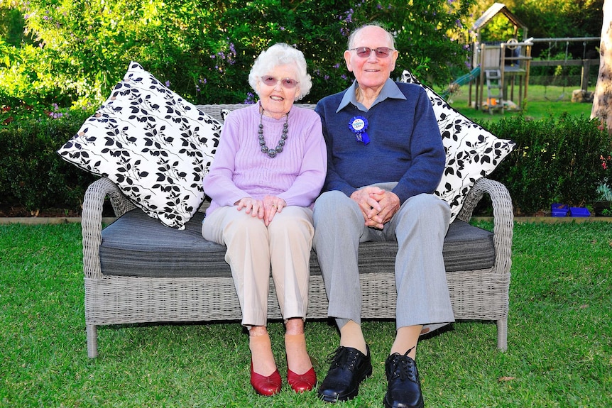 A portrait of Audrey MacGregor and her husband of 61 years, Walter sitting on a lounge in a garden.