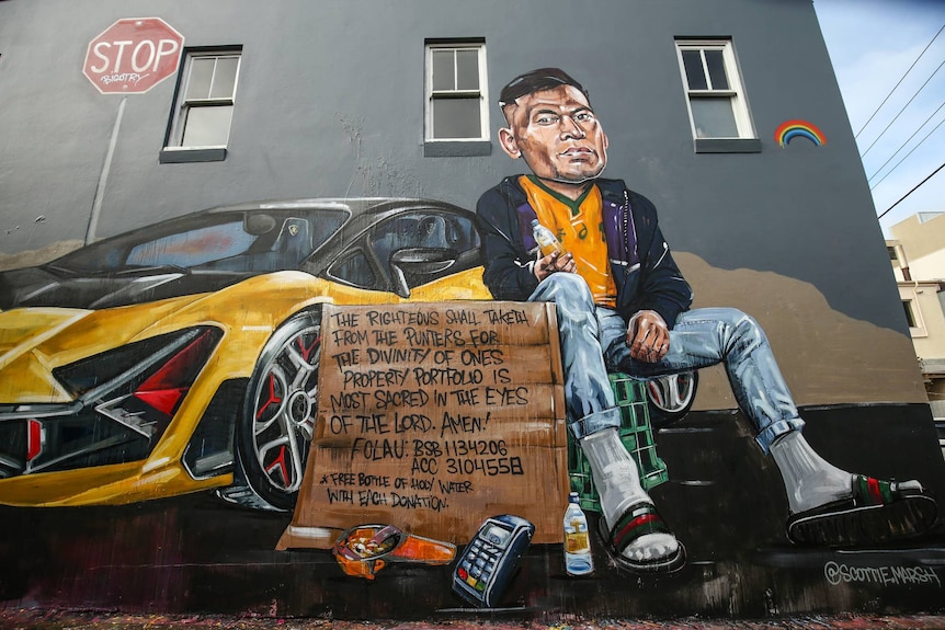 A mural of Israel Folau sitting on a dustbin next to a sports car with a cardboard sign