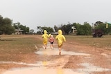 Three kids in raincoats play in puddles in the mud after recent rainfall.