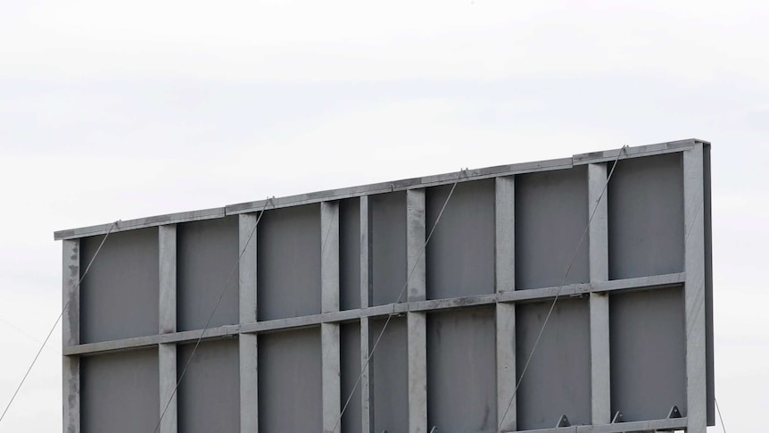 A wall with grey metal columns are topped with a large metal plate.