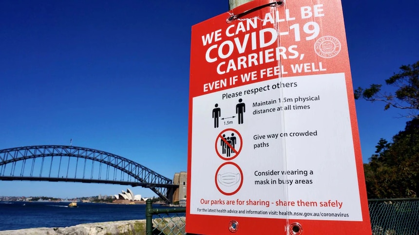 A sign about the COVID-19 pandemic against the backdrop of the Sydney Opera House