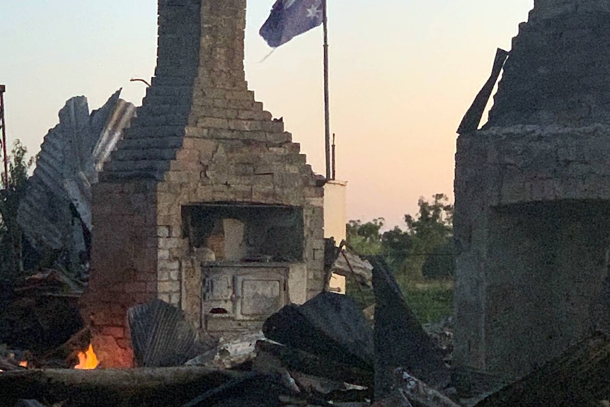 A fireplace stands amongst the burned remains of a house, with an Australian flag flying in the background