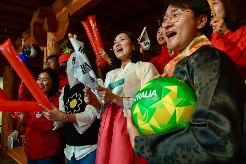 A group of South Korean football fans is cheering, with clapping sticks and flags.