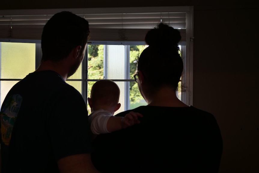The silhouette of a man and woman, holding a baby, looking out the window