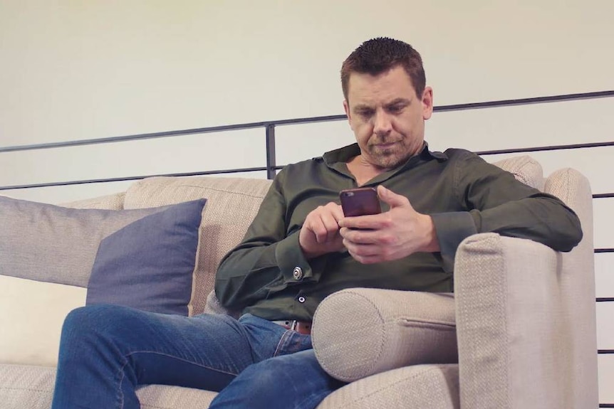 A man is sitting on a couch scrolling and looking through his phone.