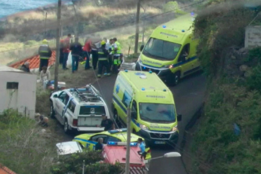 Three ambulances and emergency services crowded on a hill near a bus that has crashed.