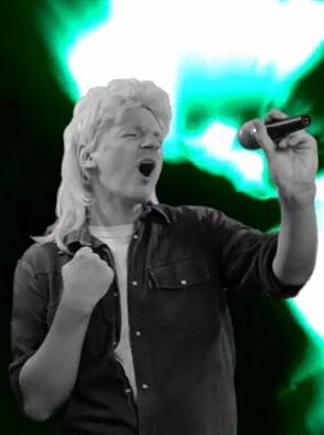 Julian Assange features in the video wearing a wig and singing a parody of John Farnham's You're The Voice.