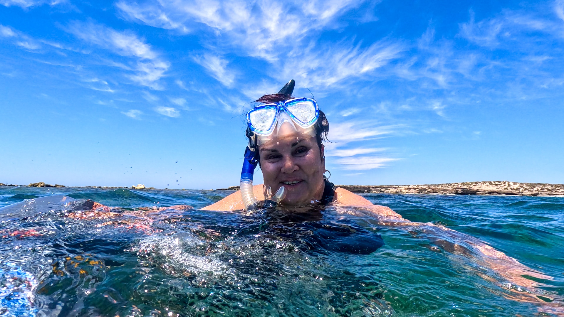 Woman wearing snorkel in the water under very blue sky.