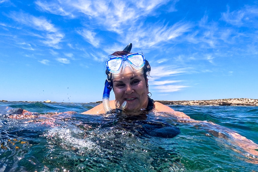 Woman wearing snorkel in the water under very blue sky.