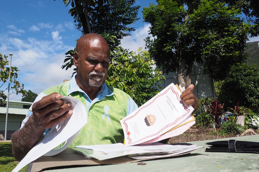 An Indigenous man with a goatee wearing a light green and blue polo flicks through documents related to his ACBF policies