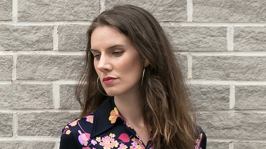 Woman with her head tilted to the side with a neutral expression against a brick wall