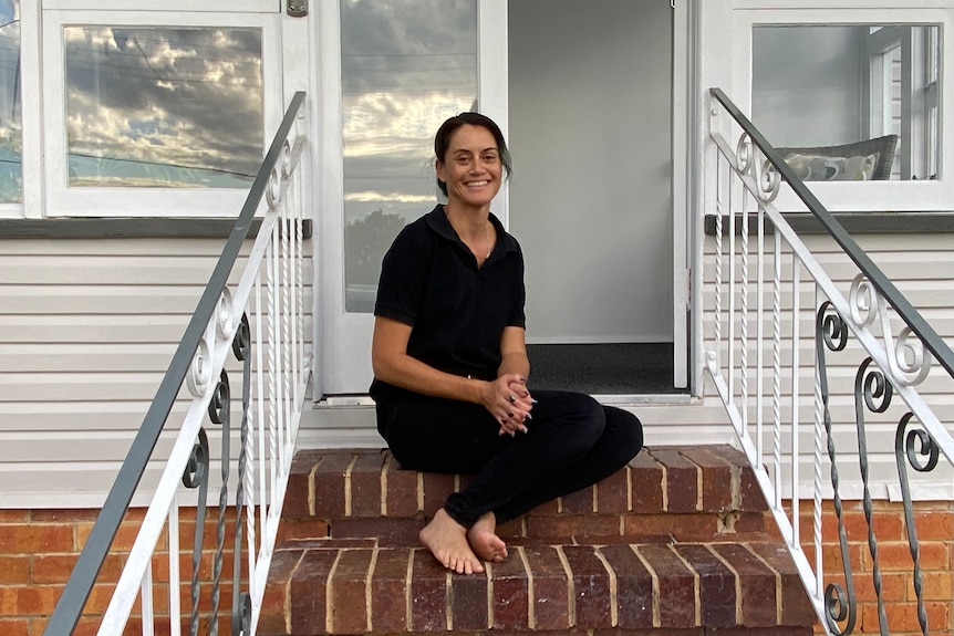 Maree Smith gives thumbs up as she sits on the steps of her first home she has bought in Ipswich.