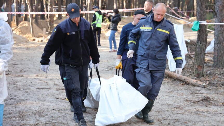 Two men carrying a body bag down a road.