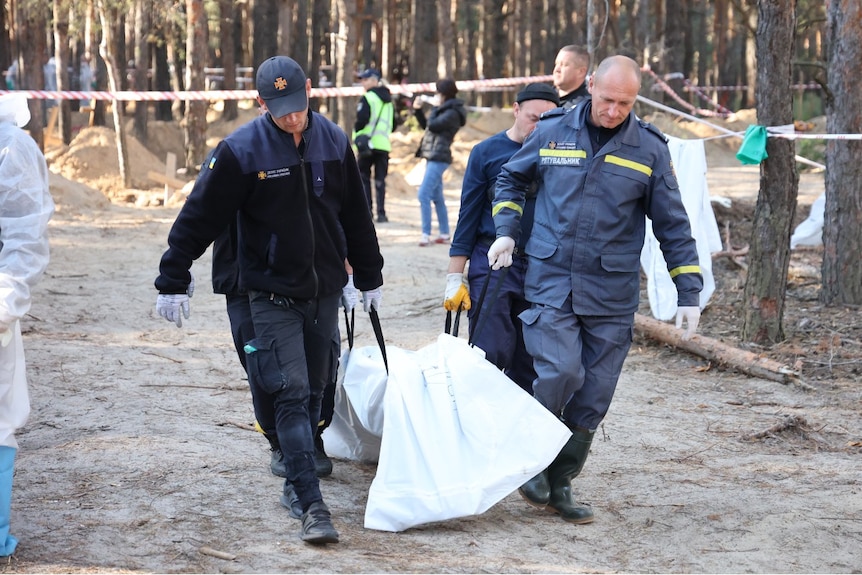 Two men carrying a body bag down a road.