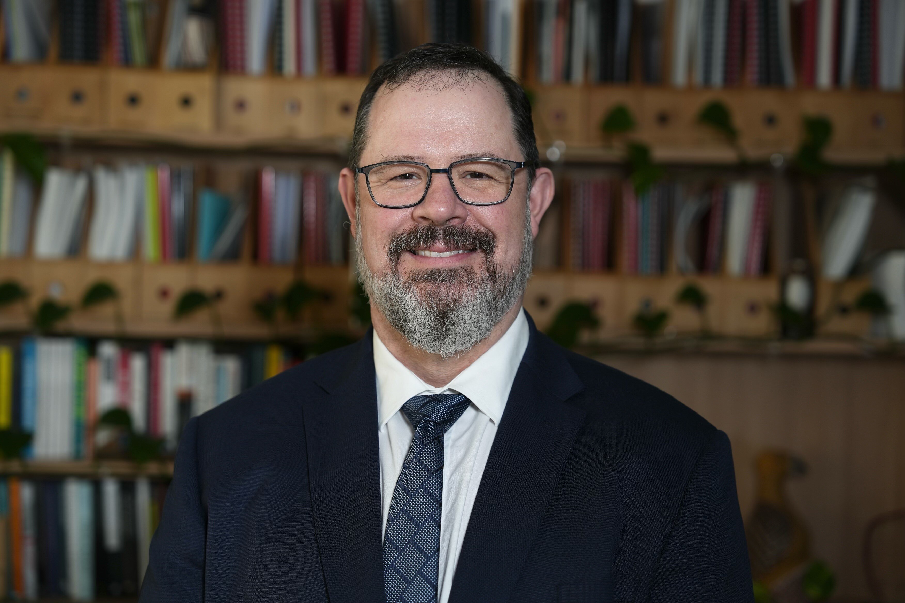 Michael dressed in a suit and tie, positioned in front of what looks to be a bookshelf.