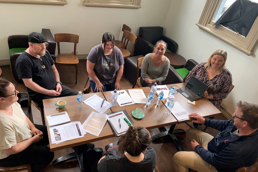 Looking down at seven people gathered around a rectangular table. 