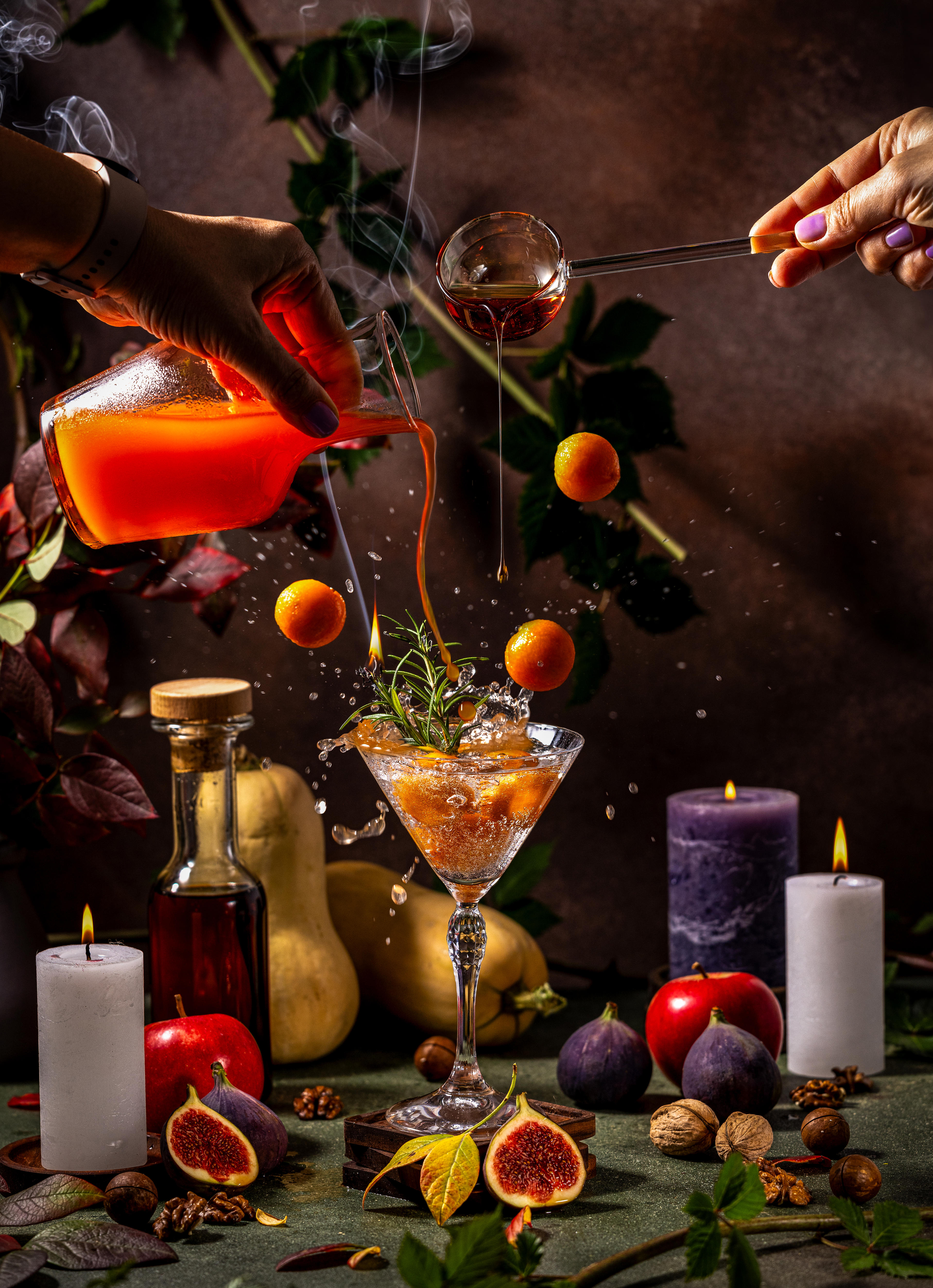 Pumpkin juice flows into a martini glass from a pitcher held above. Orange fruits float in the air around it. 