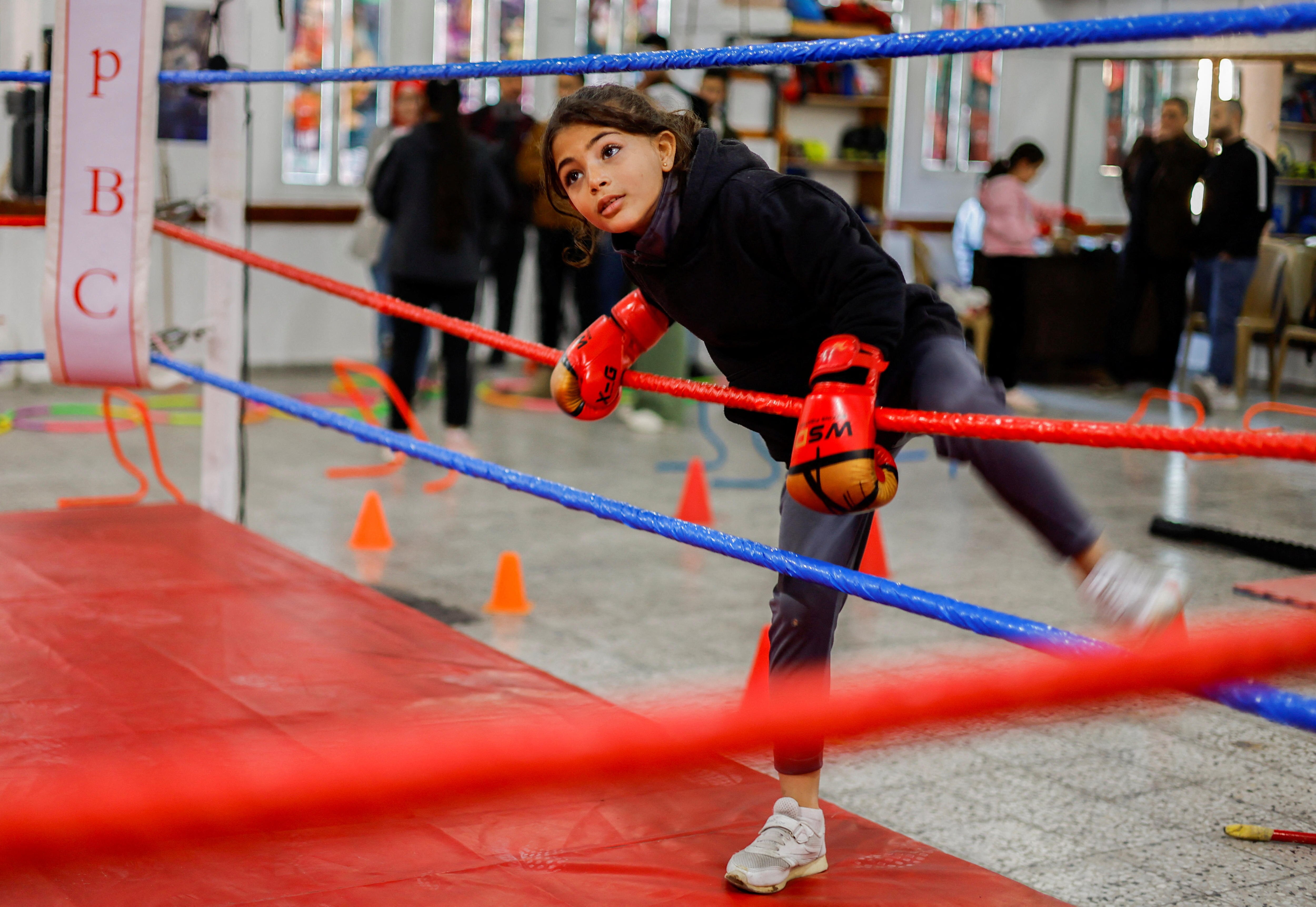 A young girl climbs between two ropes into the boxing ring. 
